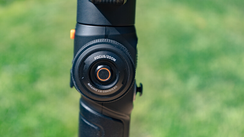 Close-up of a rifle scope mounted on a black rifle, showing the turret and reticle with blurred green background.
