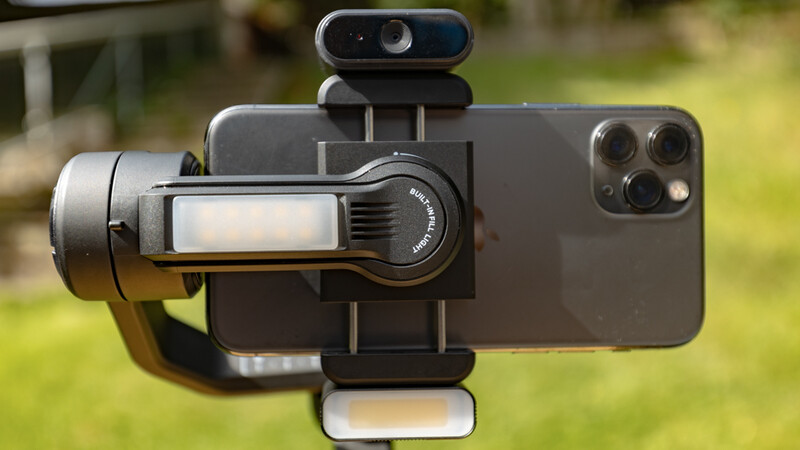Smartphone mounted on a gimbal stabilizer with external microphone and wide-angle lens adapter attached.