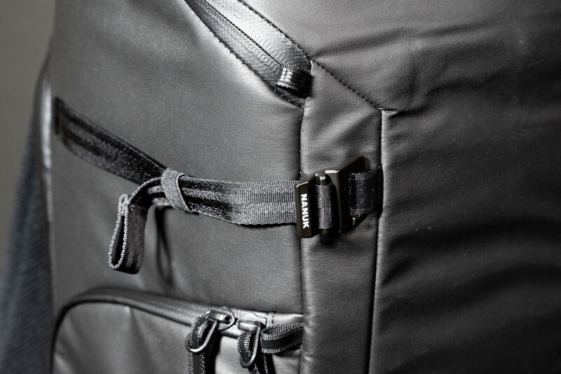 Close-up of gray backpack exterior showing multiple zippered pockets and fabric straps with metal hardware.