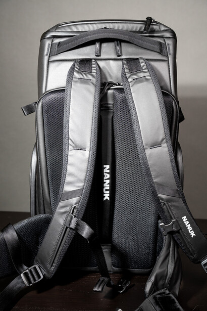 Gray and black camera backpack displayed open from behind, showing padded shoulder straps and internal compartments.
