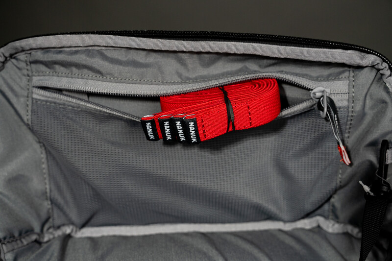 Red camera strap coiled inside a gray camera bag's zippered compartment.