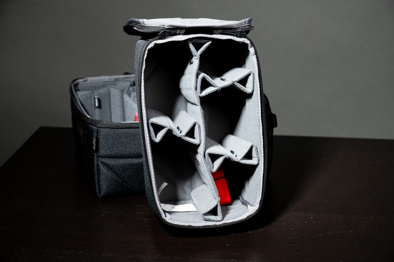 Open camera backpack with white padded dividers and a red accent strap visible inside.
