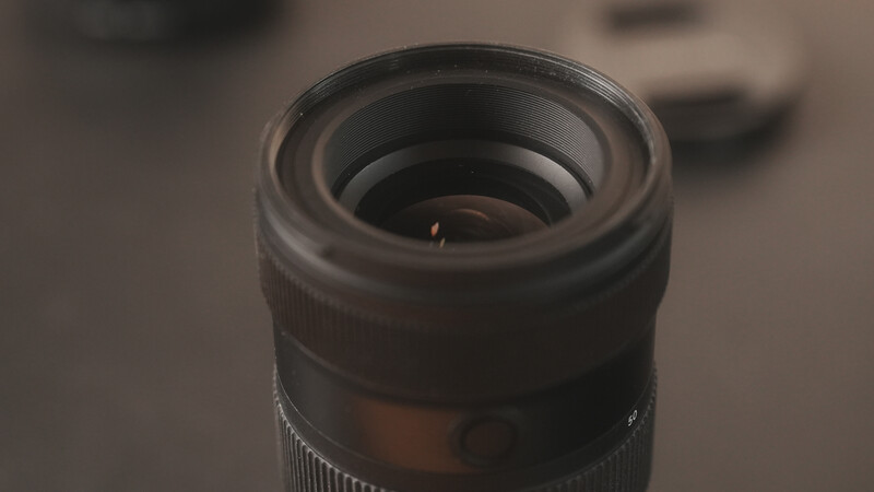 Close-up of a telephoto lens front element with shallow depth of field and warm studio lighting.