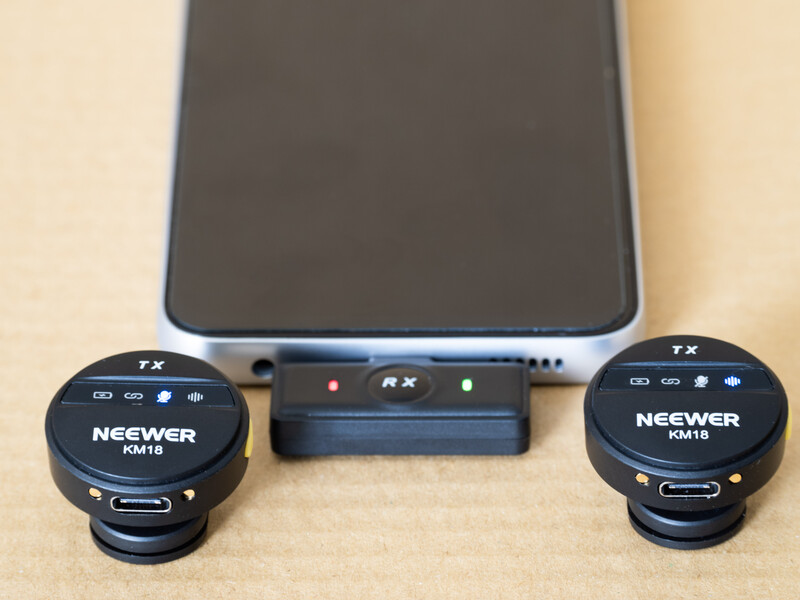 Neewer wireless microphone system with two round transmitters and a receiver unit displayed with a smartphone.