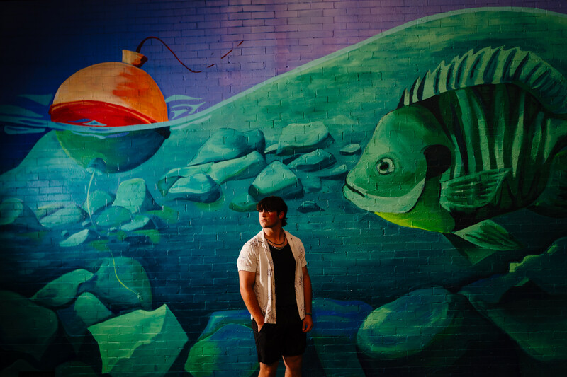 Man standing in front of large underwater mural featuring green fish skeleton and submarine.
