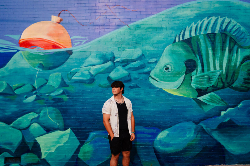Person standing in front of large-scale mural depicting underwater scene with stylized fish and rocks.