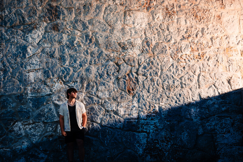 Person in light-colored shirt standing against weathered textured wall with strong shadow cast across surface.