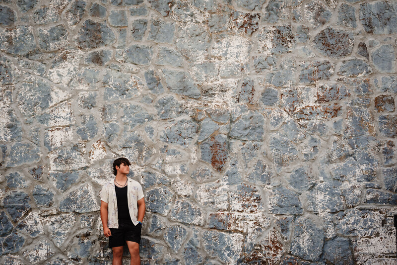 Person in casual clothing standing against a weathered stone wall with peeling paint and texture.