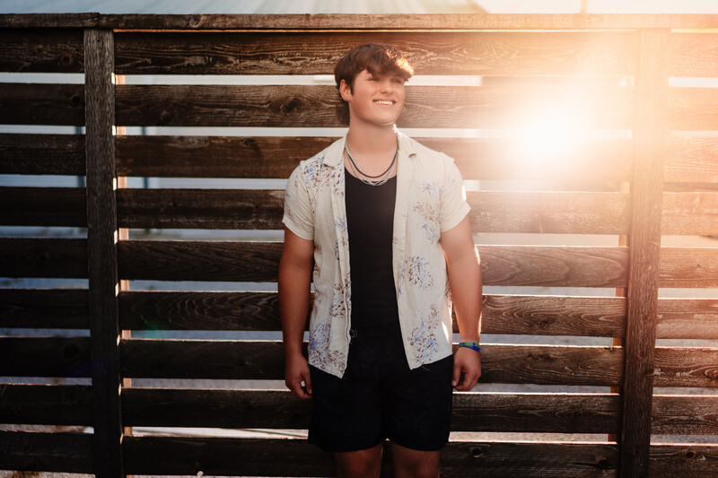 Young man in casual wear standing against wooden fence during golden hour.