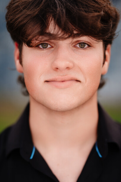 Headshot of a young man with dark brown hair and bangs, wearing a black polo shirt.