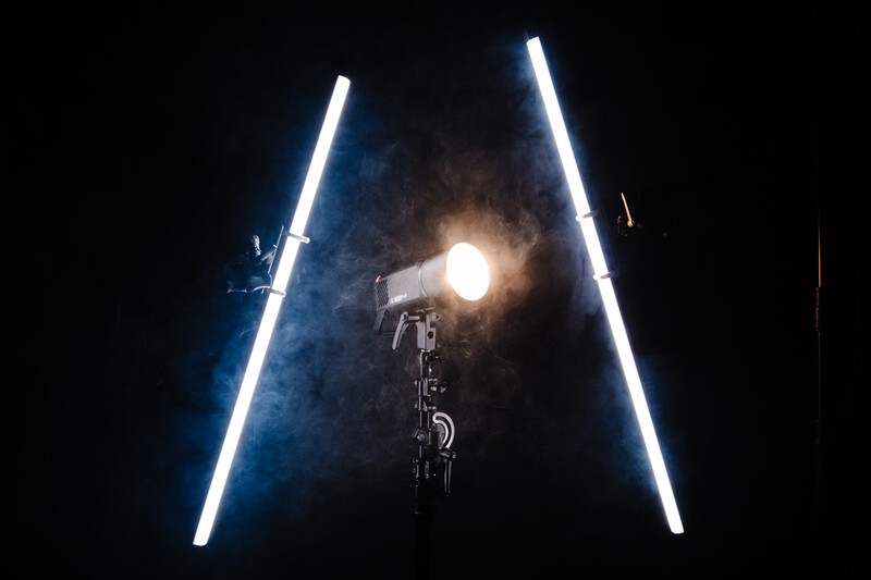 Bicycle suspended in darkness between two vertical neon blue light tubes with a bright spotlight illuminating it from above.
