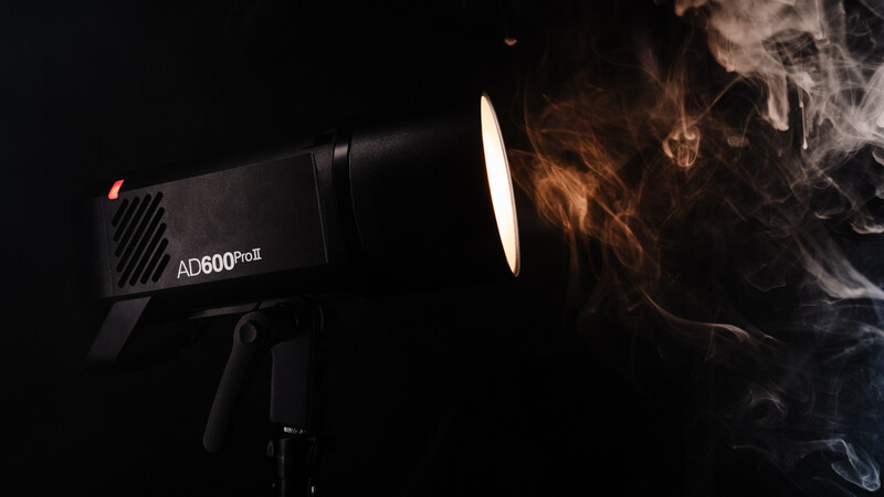 Professional LED light fixture (AD600Pro) creating dramatic warm and cool toned smoke effects against a black background.