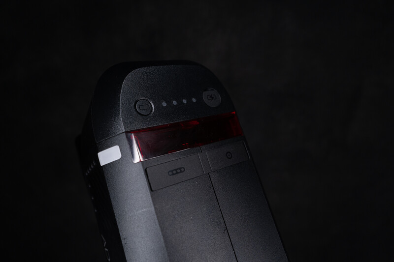 Compact camera or device with dark gray body and red accent stripe against black background.