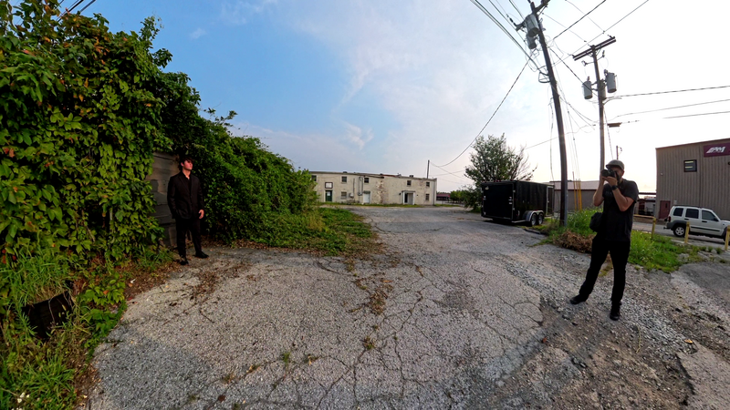 Two people in dark clothing stand on opposite sides of an industrial gravel road during golden hour.