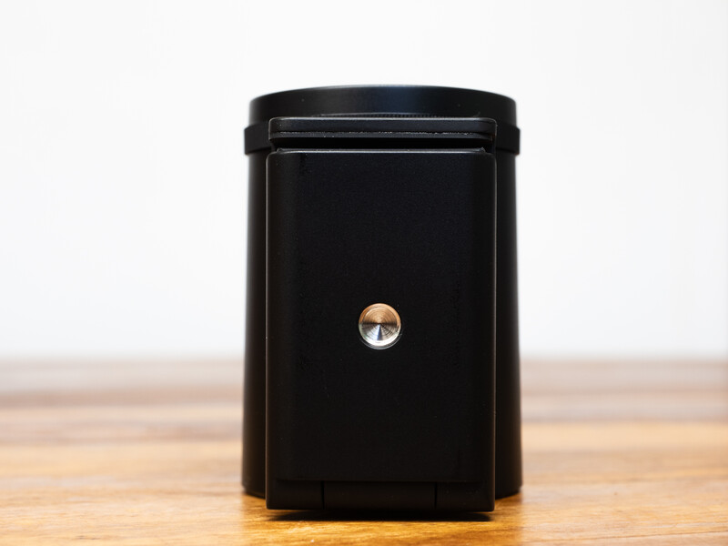 Black cylindrical container with a metallic center button on a wooden surface.