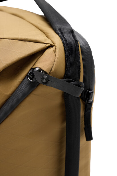 Close-up of a tan and black camera backpack showing compression straps and zipper details.