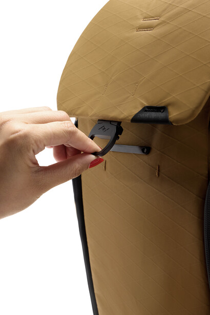 Hand inserting a black strap connector into a tan-colored camera bag or protective case.