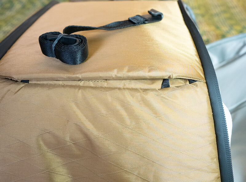 Beige camera bag or equipment case with black straps and zipper detail on outdoor surface.
