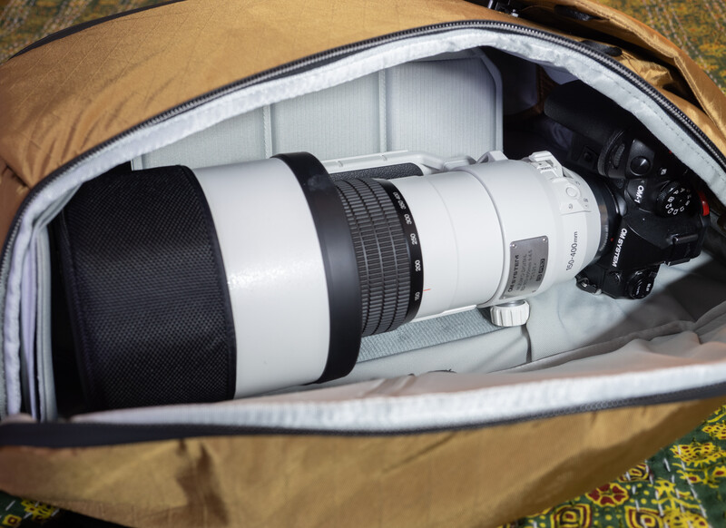 White telephoto lens and black camera body nested in a padded camera bag with tan exterior.