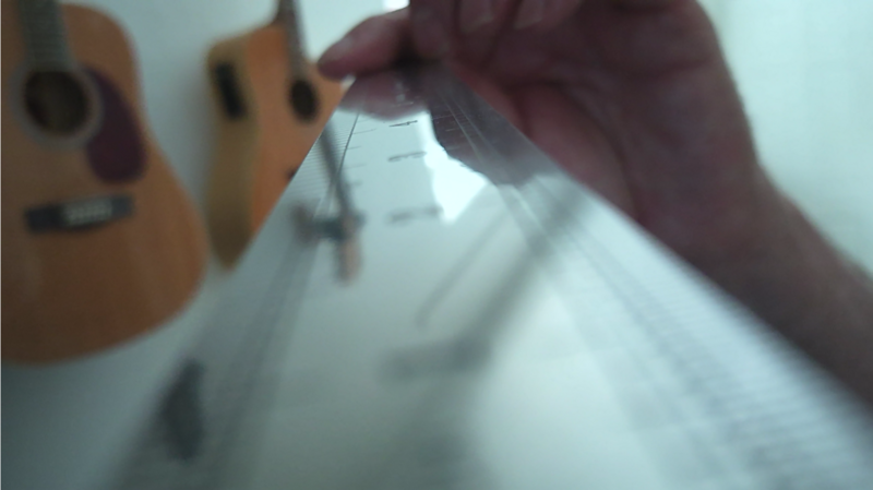 Hands adjusting strings on an acoustic guitar neck against a light background.