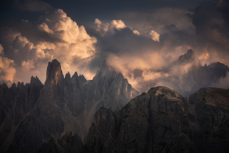 Dramatic mountain peaks shrouded in golden-lit clouds at sunset or sunrise.