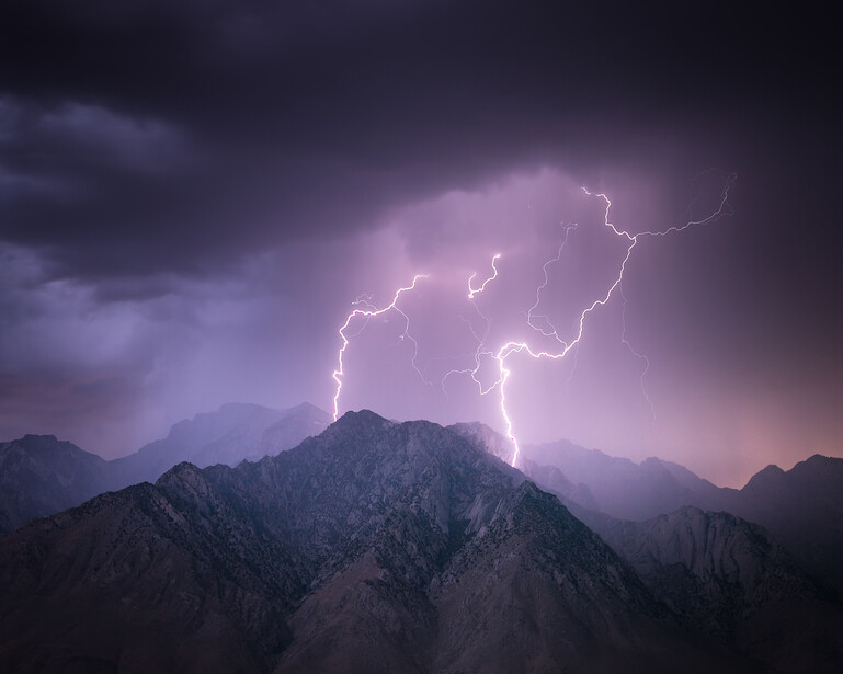 Lightning bolts striking above a jagged mountain peak during a nighttime thunderstorm.