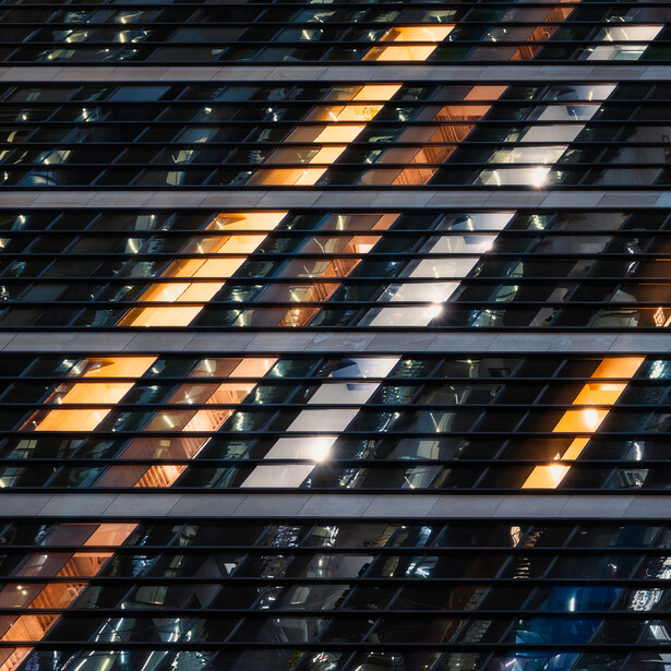 Diagonal striped pattern of illuminated building windows at dusk, with warm and cool tones creating geometric composition.
