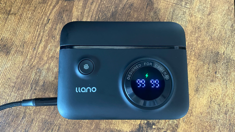 Llano portable camera monitor displaying 03:33 on its digital display, mounted on a wooden surface with power cable attached.
