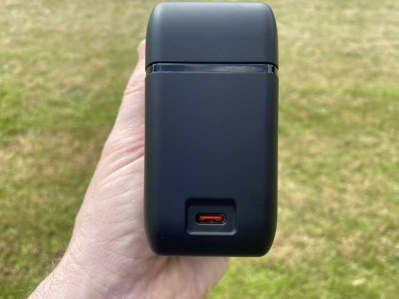 Hand holding a black portable power bank with USB-C port against blurred green grass background.