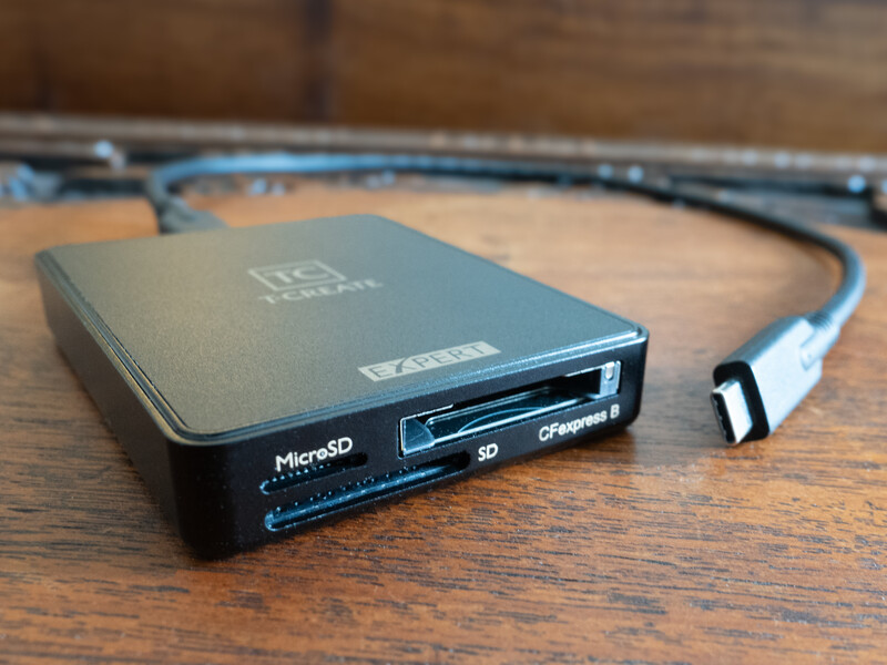 External card reader with USB cable connected, displaying MicroSD and SD card slots on wooden surface.