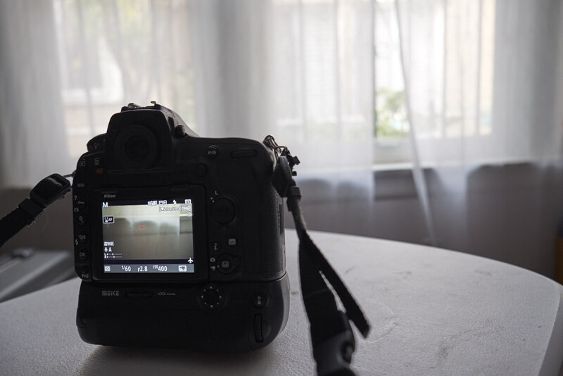 Professional DSLR camera with battery grip displayed on table indoors, LCD screen visible showing a room interior preview.