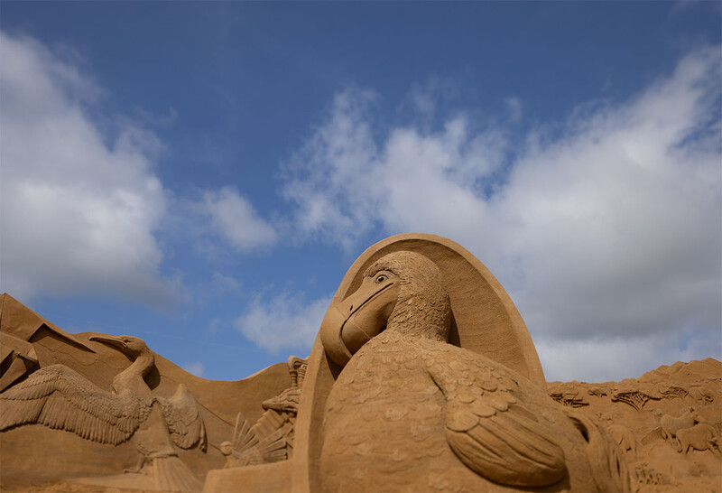 Large sandstone sculpture of an eagle's head against blue sky with white clouds.