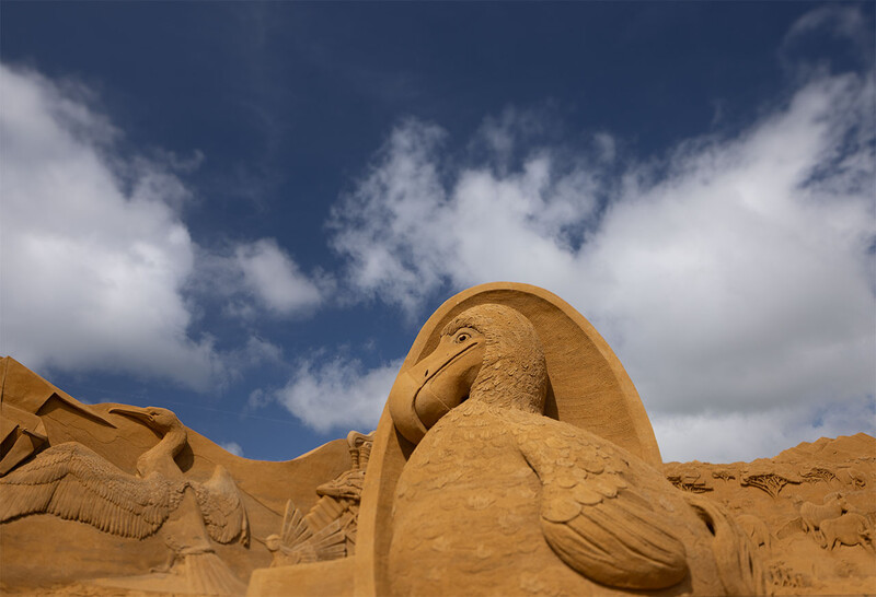 Large carved stone sculptures of Egyptian pharaohs and deities against a deep blue sky with white clouds.