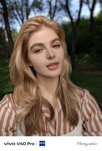 Portrait of a woman with blonde wavy hair wearing a striped button-up shirt outdoors.