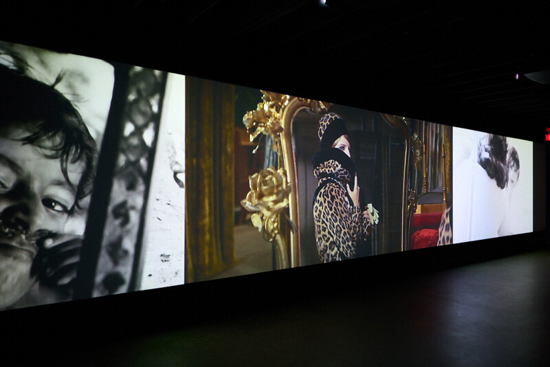 Multi-panel video installation displaying vintage glamour photography and period fashion imagery on illuminated screens in a dark gallery space.