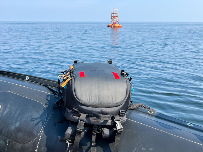 Inflatable rescue buoy secured to ship deck with calm ocean and distant navigation tower visible.