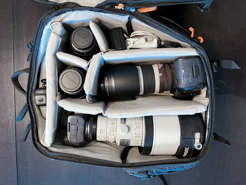 Camera backpack interior organized with lenses, camera bodies, and accessories in padded compartments.