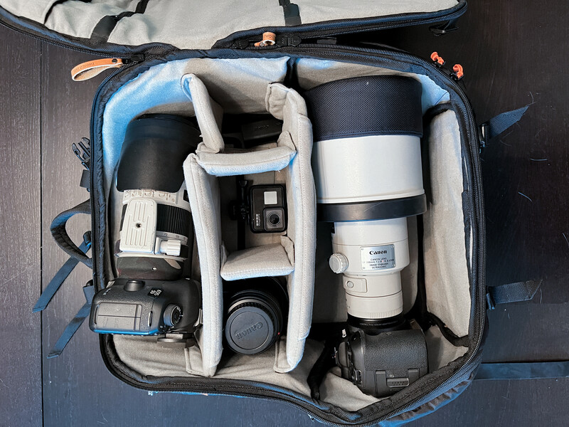 Blue camera bag with custom dividers organizing telephoto lens, DSLR bodies, and compact camera equipment.