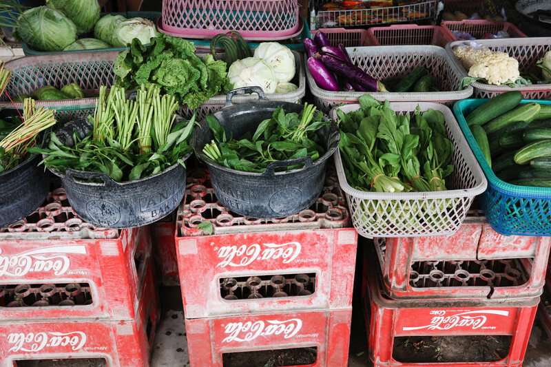 Vibrant market display of fresh leafy greens in metal bowls and woven baskets stacked on red plastic crates.