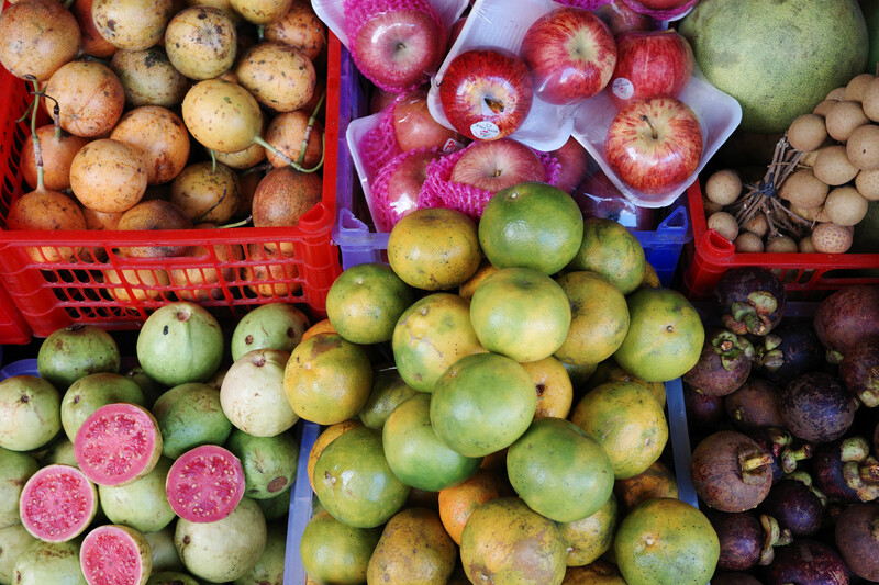 Overhead view of tropical and heirloom fruits displayed in plastic crates and containers at a market stand.