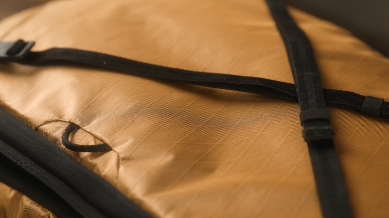 Black straps and buckles fastening a tan-colored fabric bag or pack.