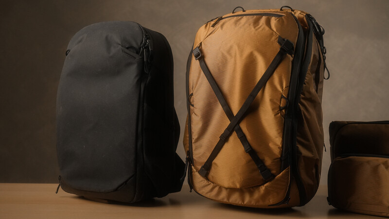 Two travel backpacks displayed side by side: a black model on the left and a tan model on the right with X-pattern compression straps.