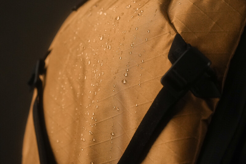 Water droplets on tan fabric under warm, side lighting with deep shadows.