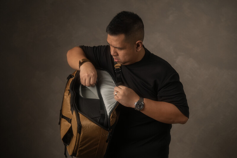 Man in black shirt examining the interior compartments of a tan and black backpack.