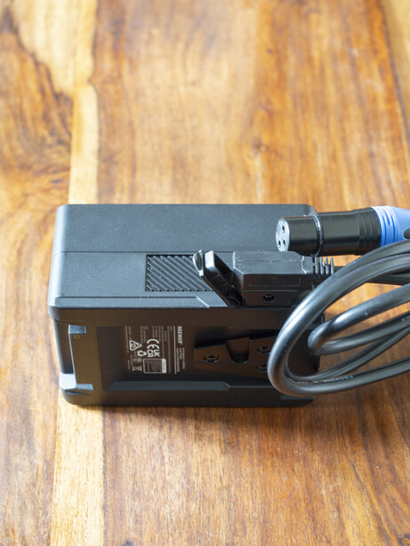 Power supply unit with blue XLR cable coiled beside it on wood surface.