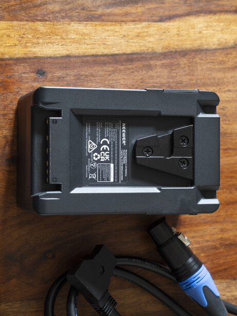 Camera flash unit mounted on wooden surface with attached power cable and blue connector.