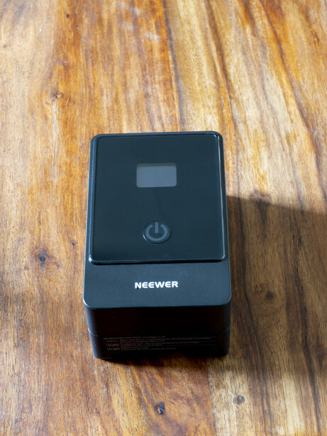 Neewer external flash power pack with LCD display and power button on wooden surface.