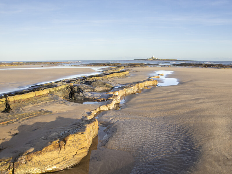 Aerial view of rocky outcrops and tidal pools on a vast sandy beach at low tide.