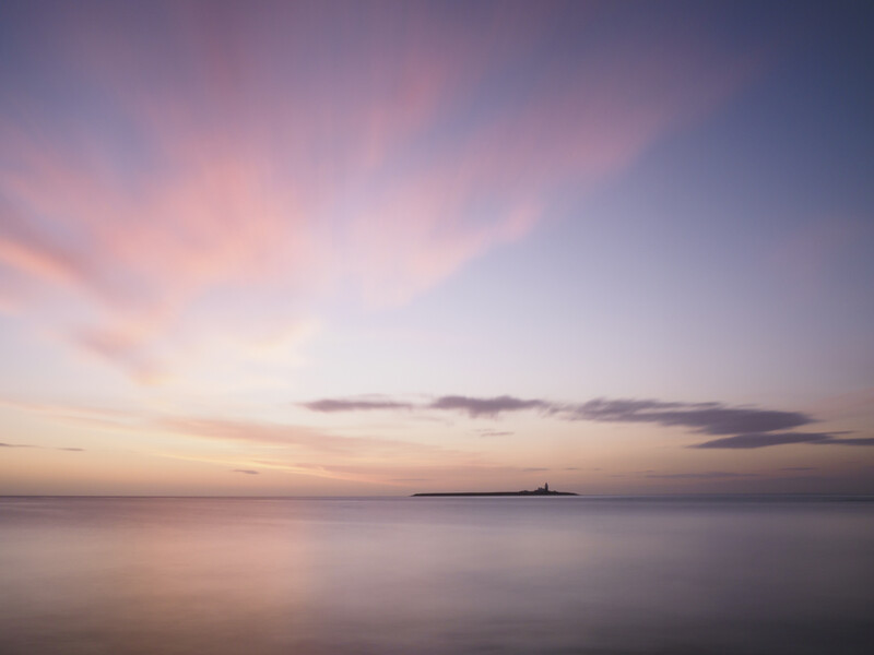 Serene seascape at sunset with calm waters and a distant silhouetted structure on the horizon.