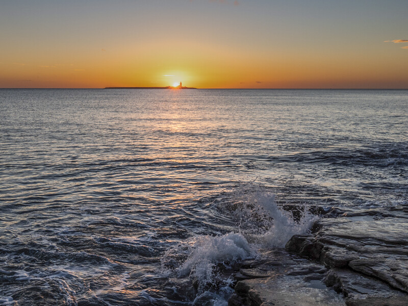 Ocean waves breaking on a rocky shore at sunset with golden light reflecting across the water.